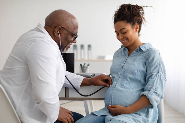 Male experienced doctor examining young pregnant woman Gynecology Consultation. Smiling black pregnant woman visiting her obstetrician doctor in maternity clinic, mature male gynaecologist examining her belly with stethoscope, doing medical check-up pregnant stock pictures, royalty-free photos & images