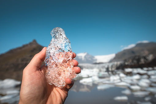 Man holding a piece of ice in his hand. Melting glacier tongue Svinafellsjokull (which is part of ice cap Vatnajokull in south Iceland) in the background.