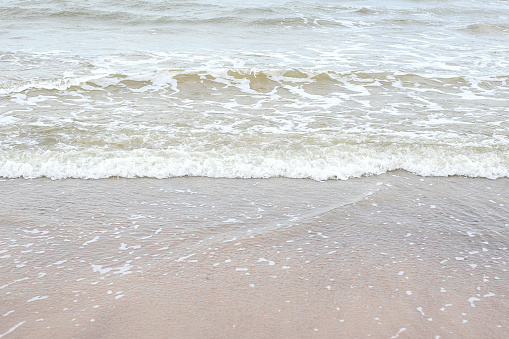 Small seaside waves near shoreline in sand.