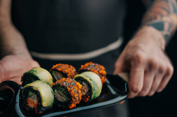 istock Man chef holds black rice sushi rolls on a cutting board. 1372114645