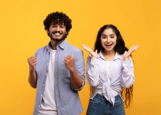 istock Wow. Overjoyed indian spouses gesturing in amazement looking at camera over yellow studio background 1372114906
