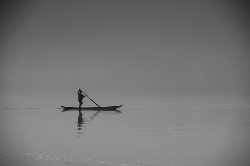 Fisherman on a misty morning paddling in a typical dugout canoue (Pirogue) on the the Maringa River in Congo. This smaller river is joining the might Congo River.