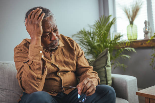 hombre maduro senior frustrado y poco saludable tocando la cabeza - sofa men adult aging process fotografías e imágenes de stock