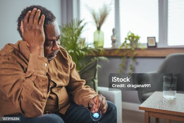 Unhappy Middle Aged Retired Grandfather Suffering From Headache Disease Indoors Stock Photo - Download Image Now