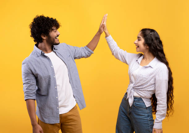 istock Common success. Young excited indian couple giving high-five, clapping hands, greeting each other over yellow background 1372115349