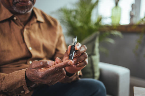 Everyday life of a man of African American nationality with a chronic disease who uses a glucose tester. A modern African man sits at a table in the living room and takes blood from his finger due to diabetes. Everyday life of a man of African American nationality with a chronic disease who uses a glucose tester. Diabetes in Men stock pictures, royalty-free photos & images