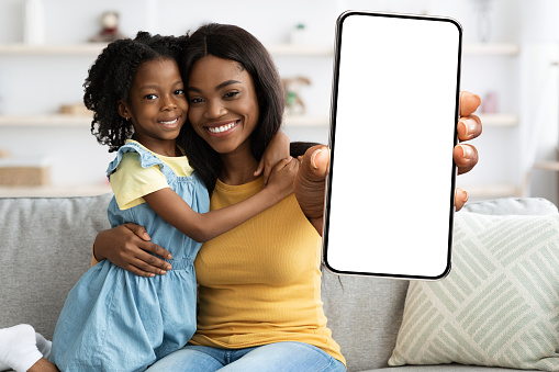Family Offer. Smiling African American Mom And Daughter Showing Blank Smartphone At Camera, Black Mother And Female Child Demonstrating Big Mobile Phone With Empty White Screen, Collage, Mockup
