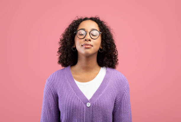 calm young black woman in glasses closing her eyes, breathing freely on pink studio background - relief bildbanksfoton och bilder