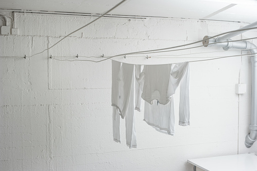 White pajamas or clothing hanging from drying lines inside communal laundry room inside apartment building. No people.