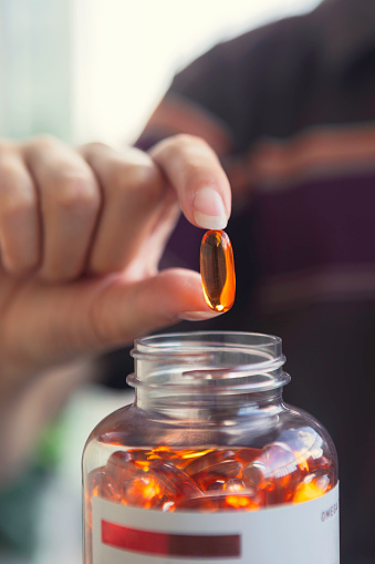 Close up of a person taking a fish oil capsule from a jar.