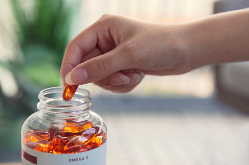 Close up of a person taking a fish oil capsule from a jar.