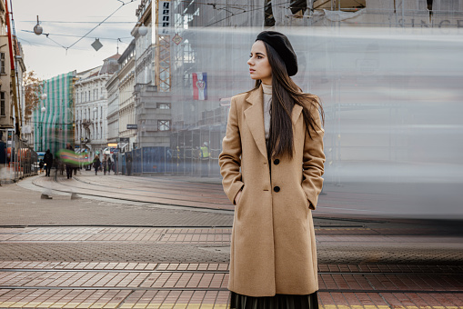 Young woman standing with hands in pockets on street against moving tram