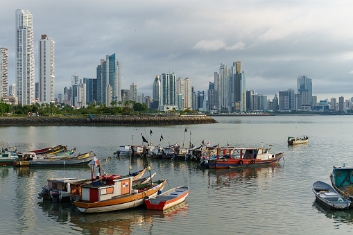 Fishing boats docked in front of modern skyscrapers in Casco Viejo Panama City. Hazy day with calm waters.