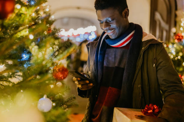 istock African American young man using mobile phone while holding Christmas gift 1372124989