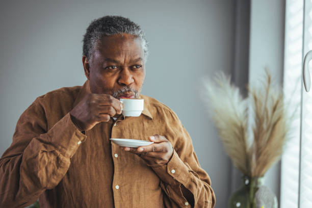 un vieil homme africain solitaire à la retraite avec une tasse de café blanche - homme mug regarder dehors photos et images de collection
