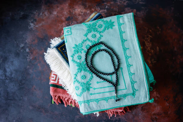 A rosary with black beads on folded prayer rugs on a brown-black rust effect concrete floor, Flat lay