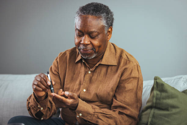 hombre mayor afroamericano que usa lanceta en el dedo para verificar el nivel de azúcar en la sangre mediante un medidor de glucosa - diabetes home interior blood sugar test healthcare and medicine fotografías e imágenes de stock