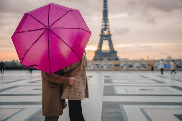 romantic couple standing on parvis des droits de l'homme, paris in front of eiffel tower holding pink umbrella - paris france eiffel tower love kissing imagens e fotografias de stock