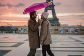 Romantic couple flirting at Parvis des Droits de l'Homme, Paris in front of Eiffel Tower, holding umbrella