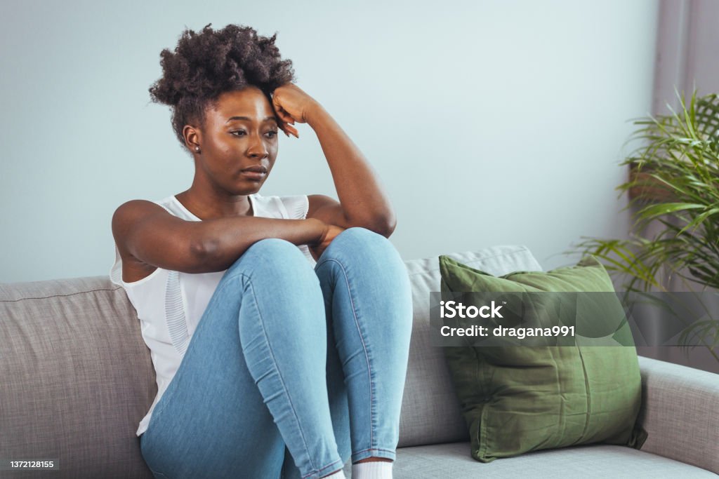 Psychology, solitude and people Unhappy lonely depressed woman at home, she is sitting on the couch and hiding her face on a pillow, depression concept. Psychology, solitude and people Women Stock Photo