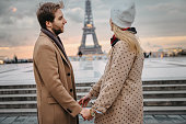Couple holding both hands, man is looking at his girlfriend, Eiffel Tower in background