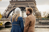 Close-up, young couple standing in front of Eiffel Tower, Paris, in the evening, man looking at his girlfriend