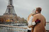 Couple hugging while standing at Seine River looking at Eiffel Tower, Paris, rear view