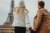Close-up of couple looking at Eiffel Tower Paris while holding hands and walking over a bridge