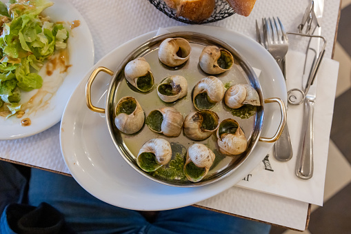 Traditional tasty French snail dish served on a silver plate standing on a table with salad and cutlery next to the dish in a fancy restaurant in Paris, top view, horizontal