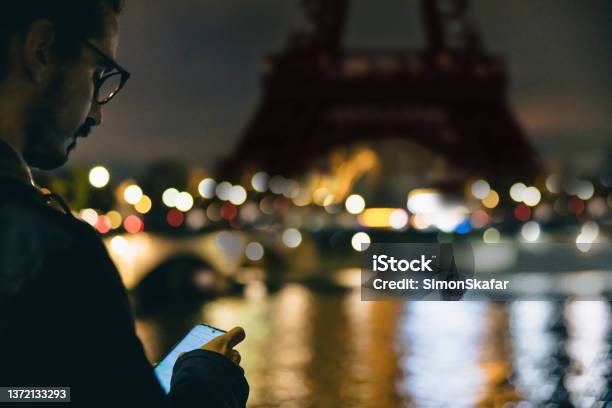 Closeup Of Man Looking Down At His Smartphone In Front Of Eiffel Tower Paris In The Evening Stock Photo - Download Image Now