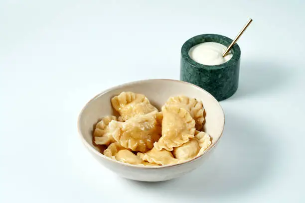 Dumplings with different fillings in a bowl with sour cream on a white background. Varenyky