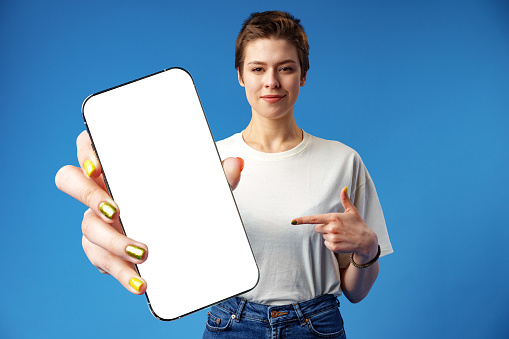 Happy woman shows blank smartphone screen against blue background, close up