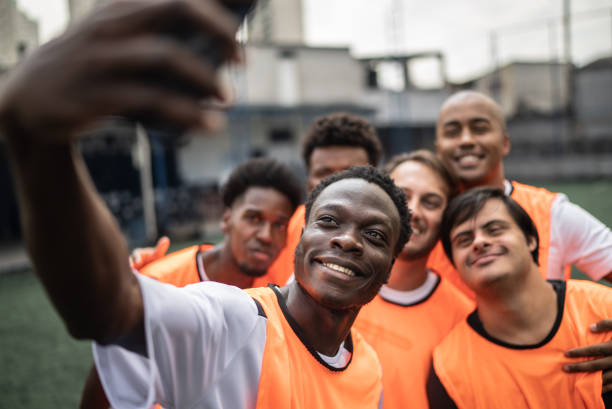 joueurs filmant ou prenant des selfies sur le terrain de football - y compris une personne ayant des besoins spéciaux - soccer player soccer men smiling photos et images de collection