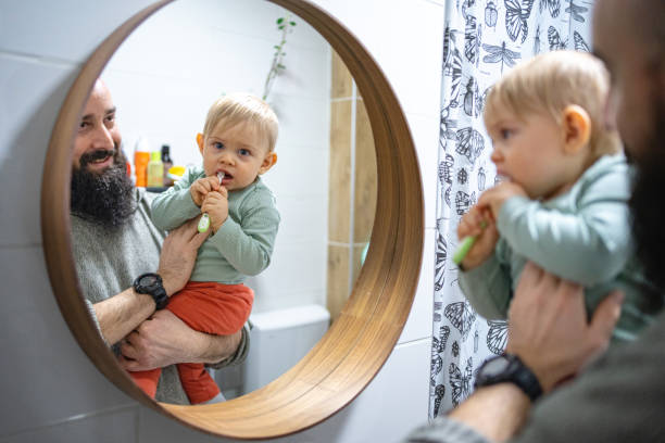 istock Toddler boy looking himself in the mirror, brushing his teeth while father holding him 1372137157