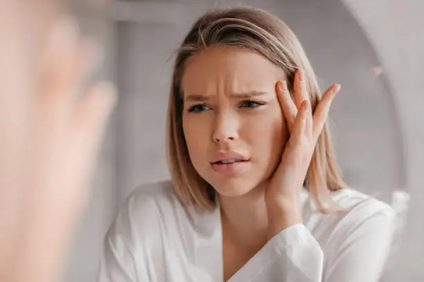 Photo of Mirror reflection of upset lady looking at mirror and touching her forehead, having dry skin problem, first wrinkles
