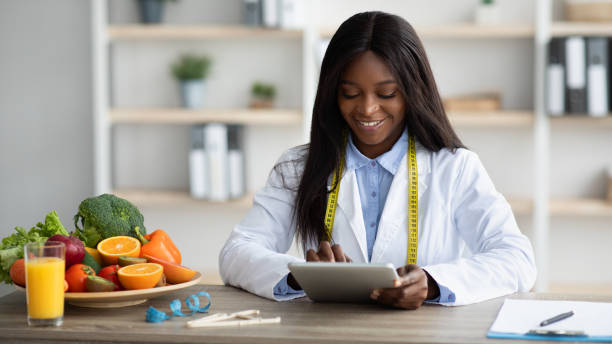 istock Young blck female dietitian working with tablet computer, giving online consultation or creating diet plan at office 1372138308
