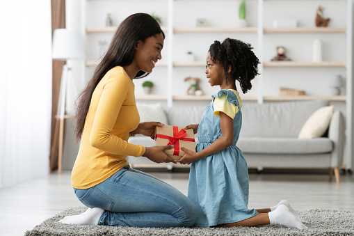 Excited Black Woman Receiving Present For Mother's Day From Her Little Daughter, Cute African American Female Child Surprising Mom With Gift While They Spending Time Together At Home, Free Space
