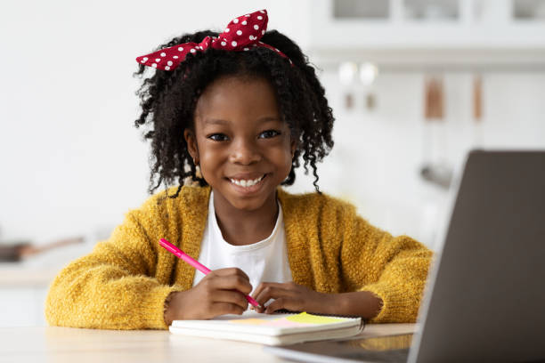 istock Cute Black Girl Writing With Pen In Notepad And Smiling At Camera 1372138744