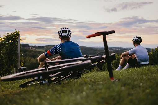 Cyclist sitting next to bicycles and enjoying the view in the vineyard at sunset.