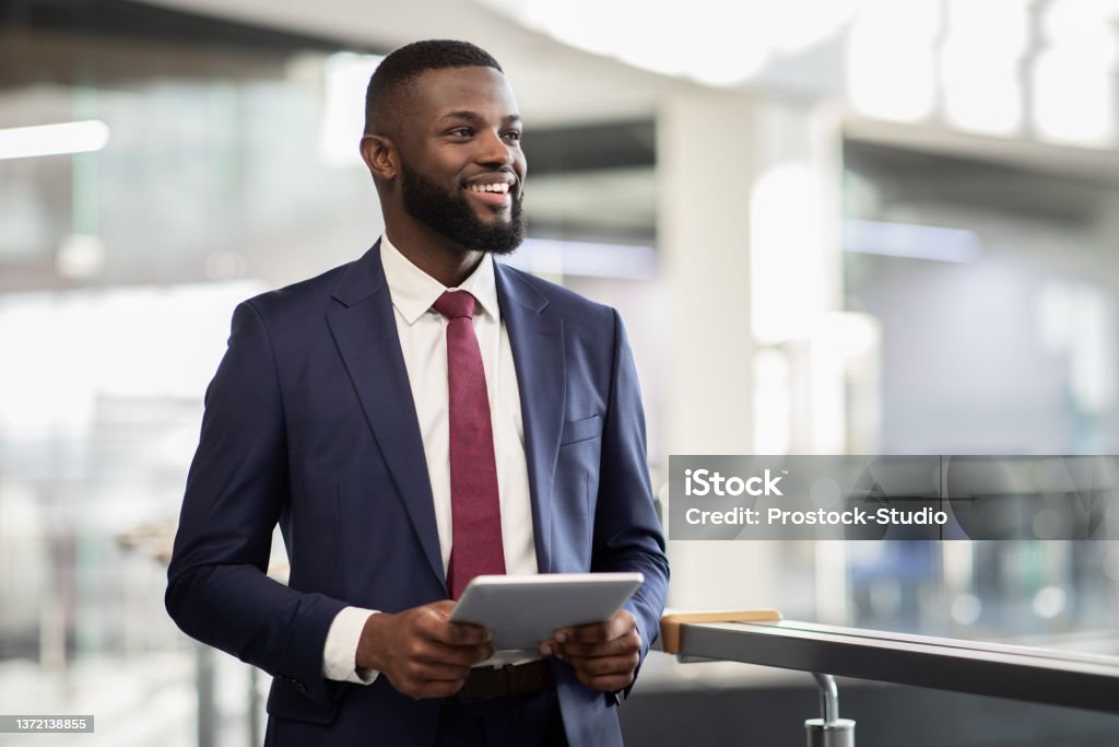 Cheerful black manager with digital tablet walking by office Cheerful young black bearded man manager walking by office building corridor, holding modern digital tablet, using mobile app for business, looking at copy space and smiling, panorama Businessman Stock Photo