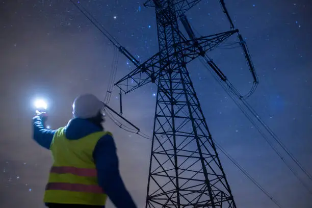 Electricity engineer working on Electrical Pylons Translation, checking the condition of the Electrical Power Pole components at night.