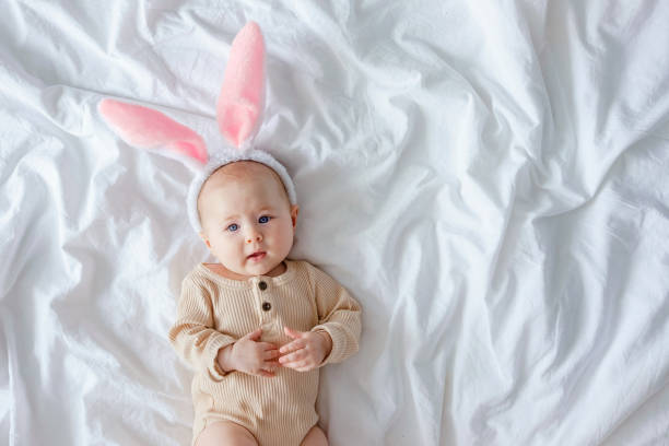 istock Dressed up for Easter. A cute funny baby with bunny ears costume dressed up for Easter laying on white bed linen sheet. 1372141169