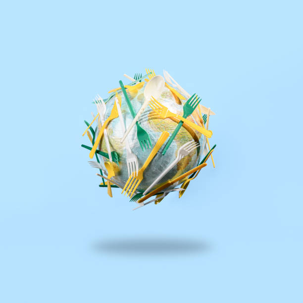 Earth globe is fully covered with disposable plastic knives, spoons, and forks. Levitating in air object over pastel blue background. Concept of the problem of plastic pollution stock photo