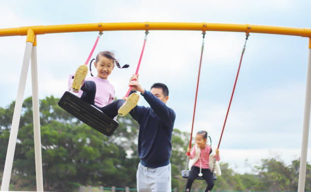 istock a father playing swings with his twin daughters. 1372143165