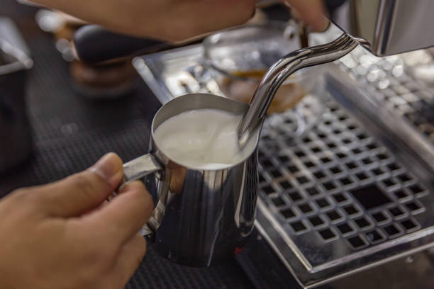 barista steaming stainless cup milk in coffee bar.