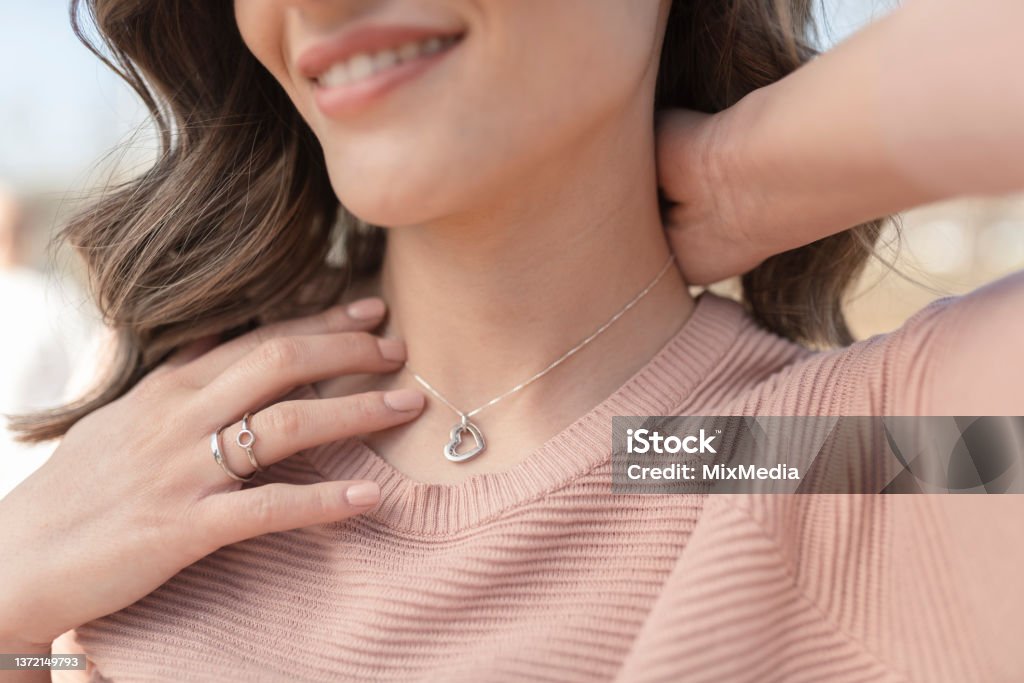 Close-up shot of a happy, beautiful woman putting on the silver necklace Close-up shot of a beautiful young woman wearing beautiful silver necklace and rings Jewelry Stock Photo
