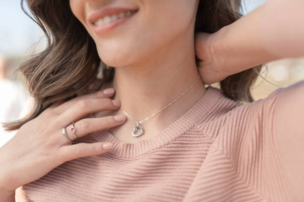 Close-up shot of a happy, beautiful woman putting on the silver necklace Close-up shot of a beautiful young woman wearing beautiful silver necklace and rings pendant stock pictures, royalty-free photos & images