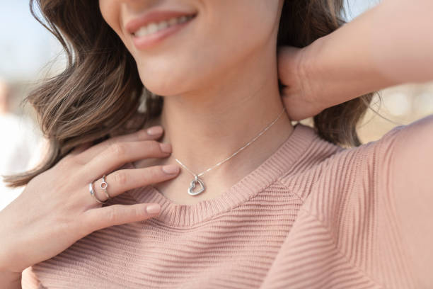 Close-up shot of a happy, beautiful woman putting on the silver necklace Close-up shot of a beautiful young woman wearing beautiful silver necklace and rings necklace stock pictures, royalty-free photos & images