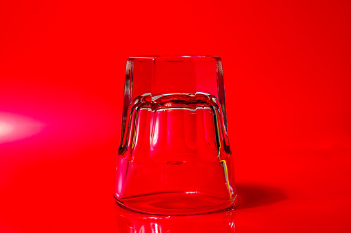 A close-up of a small glass shot glass upside down on a red gel background.