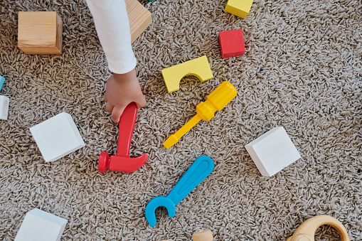 Above view of unrecognizable toddler taking toy hammer from carpet while playing with toy tools